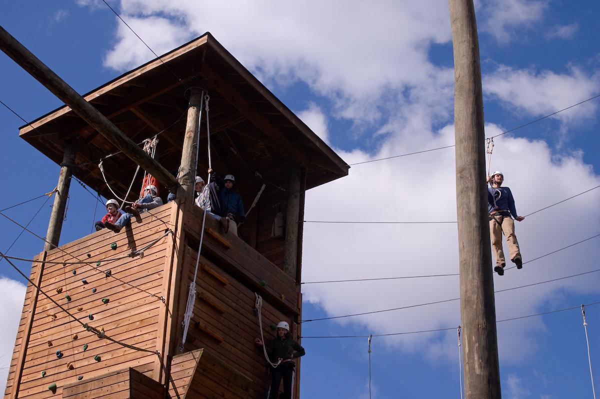 Students sit in a high ropes course tower, atop a rock wall at Ohio University